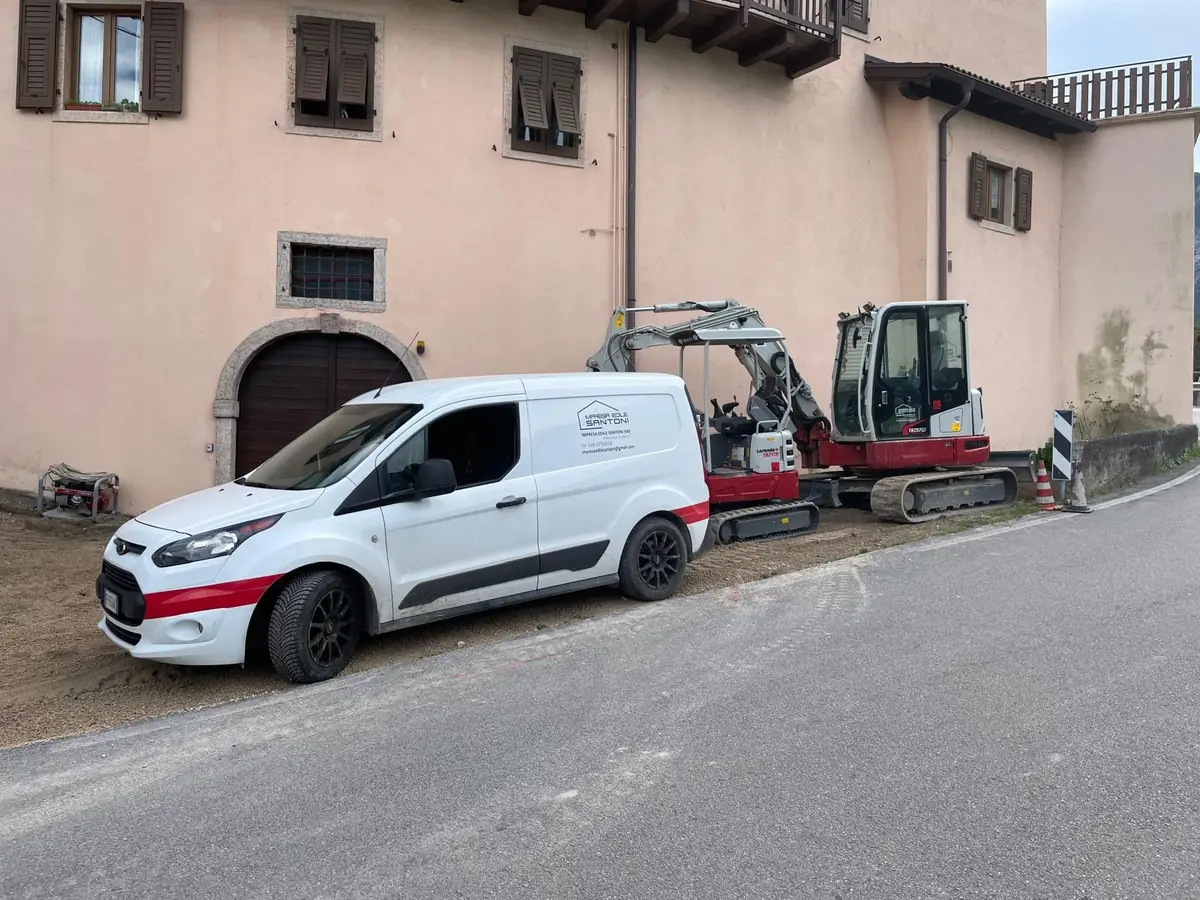 Furgone aziendale ed escavatore davanti a un edificio storico