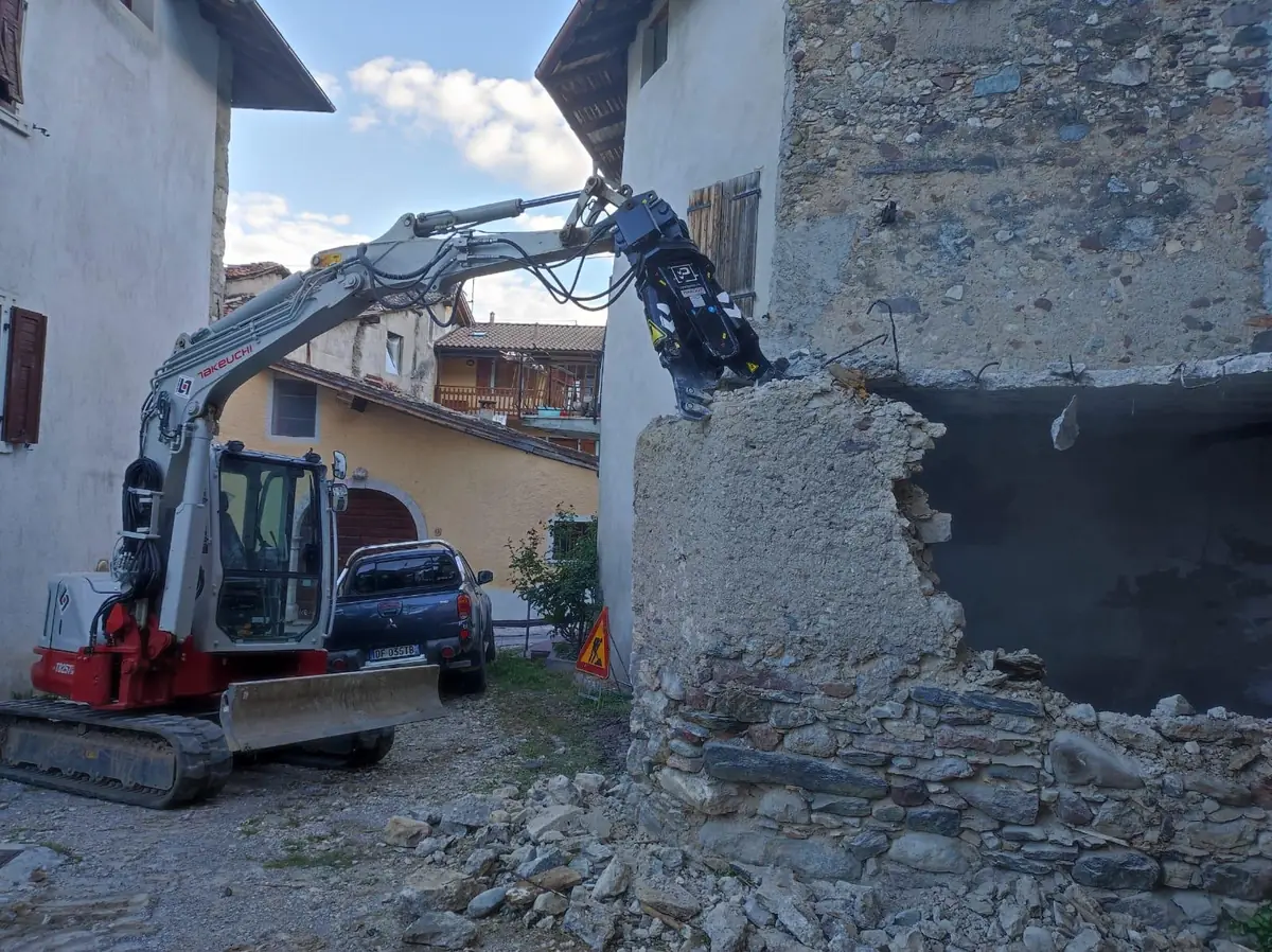 Escavatore con pinza demolitrice al lavoro su un vecchio muro in pietra